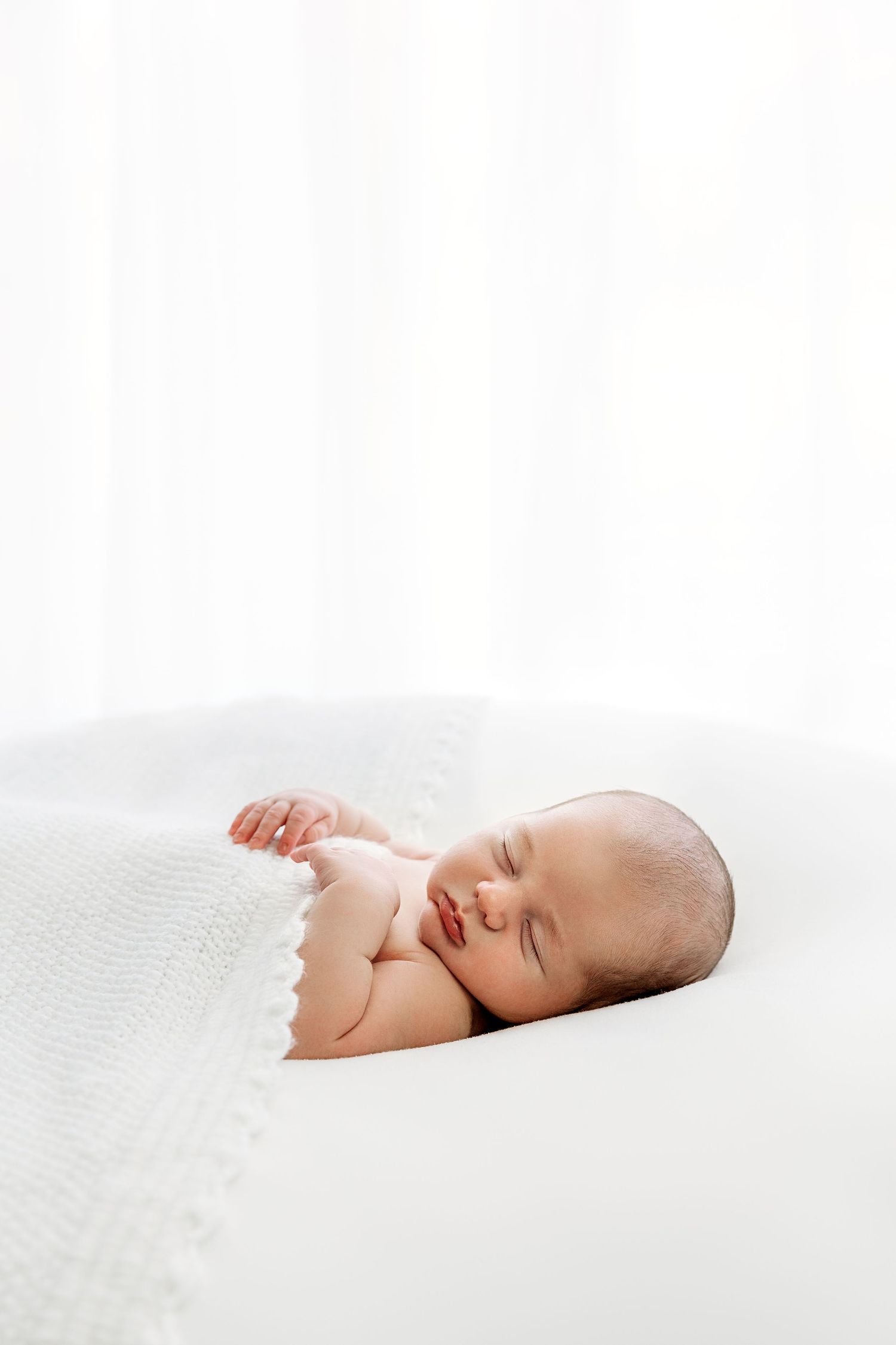 Newborn laying under heirloom knit blanket, backlit by window