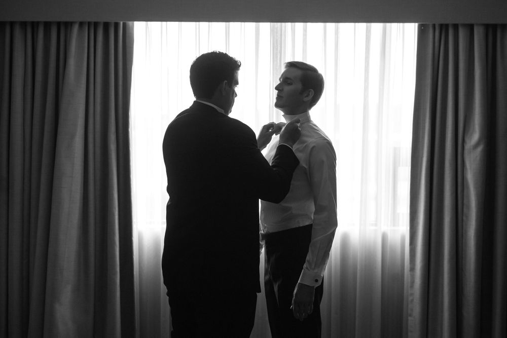 Best man helps groom with bowtie before wedding ceremony in Akron, Ohio.