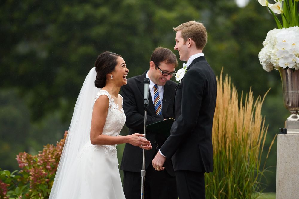 bride and groom laugh while exchanging rings during outdoor wedding ceremony at Fairlawn Country Club in Akron, Ohio.