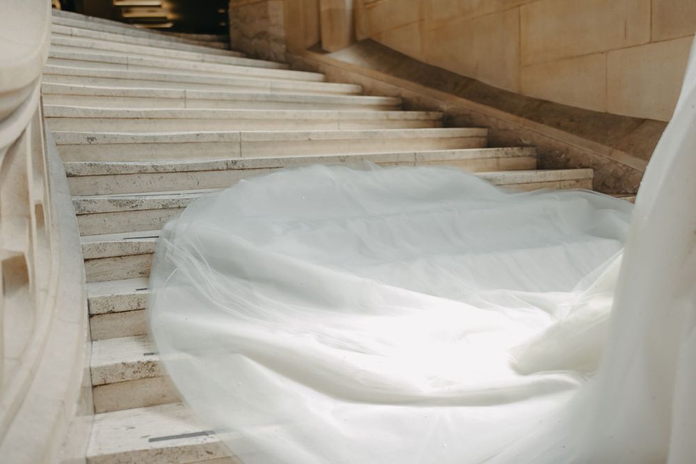 Flowing white wedding dress train cascades down marble staircase.