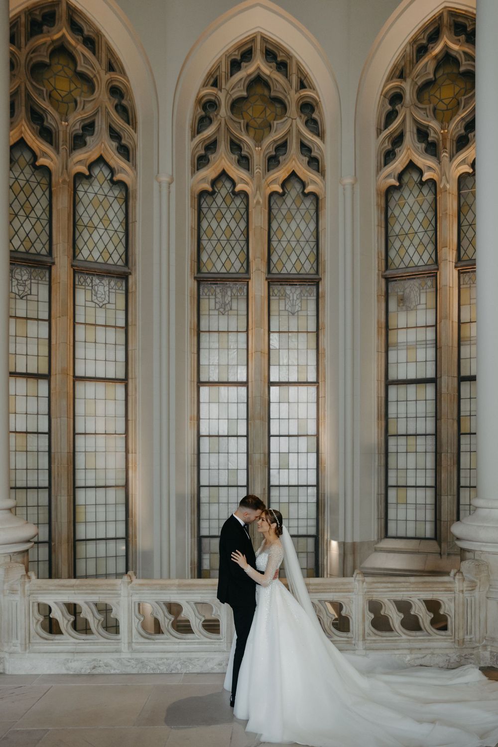 Elegant wedding portrait in front of ornate cathedral windows with gothic architectural details.