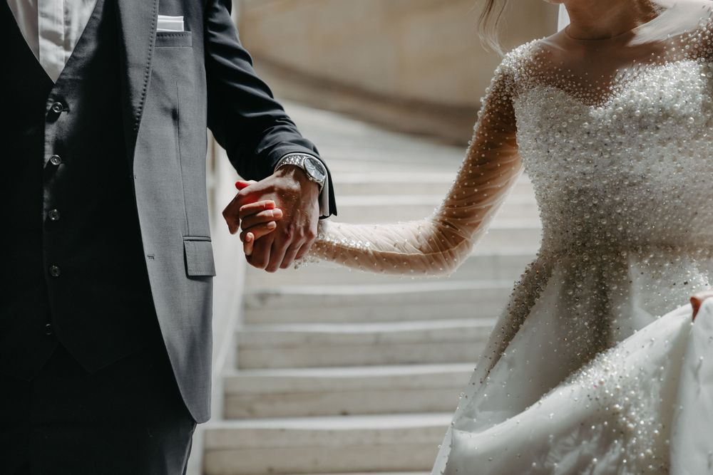 Close-up detail of newlyweds holding hands on marble stairs.