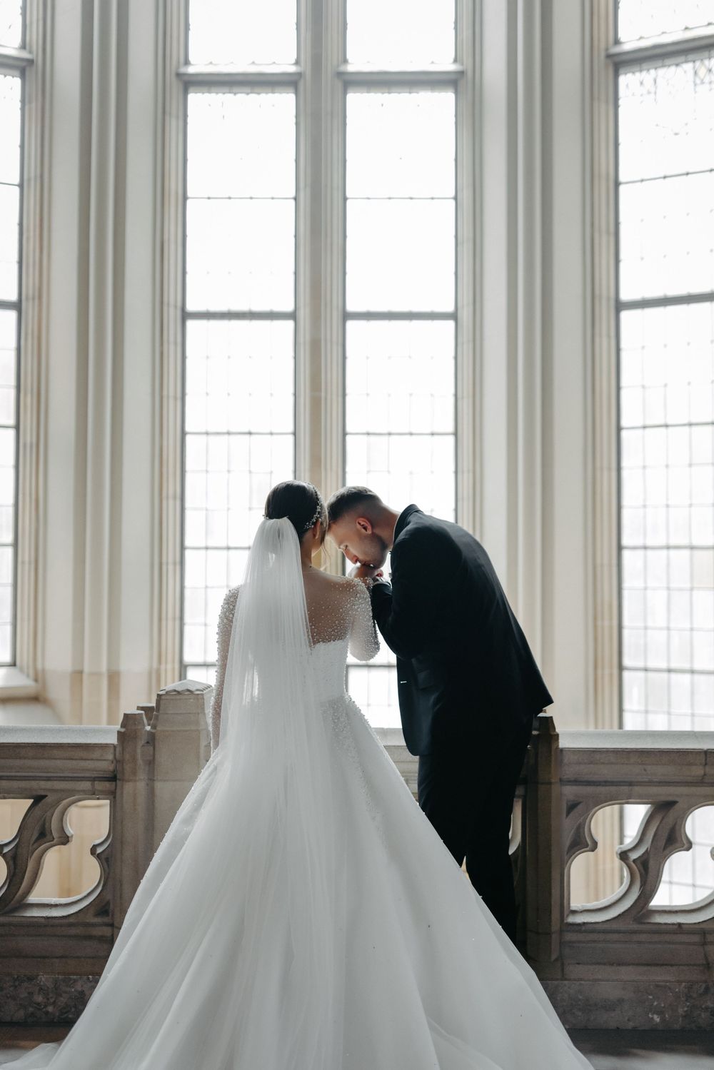 Intimate wedding moment captured by tall windows in historic building.