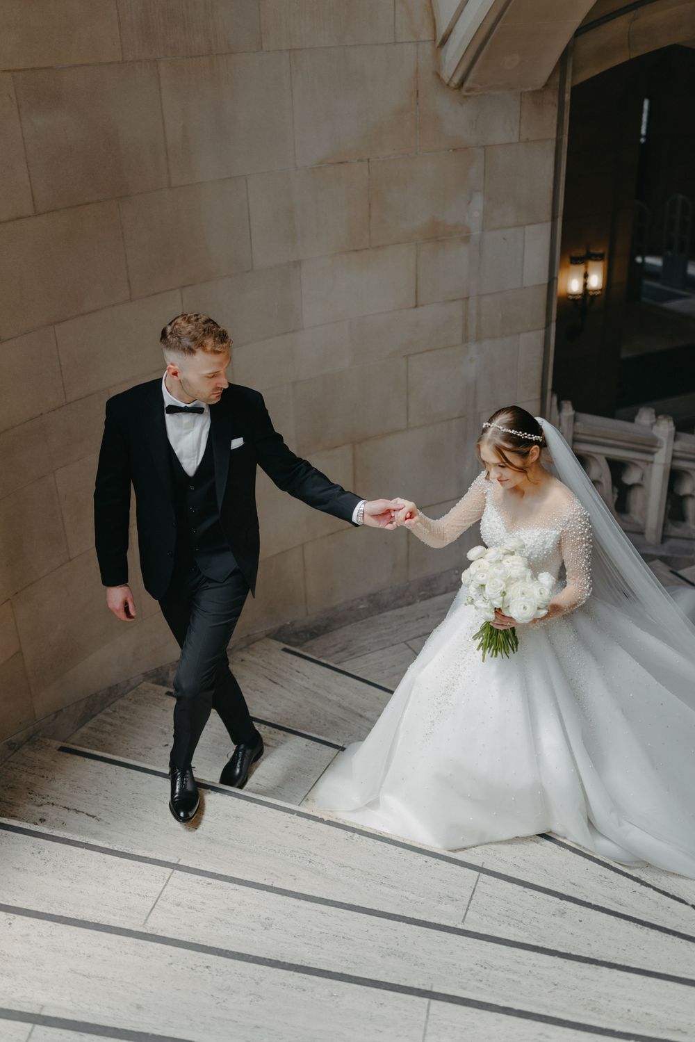Newlyweds descending stone steps with bride in flowing gown holding white bouquet.