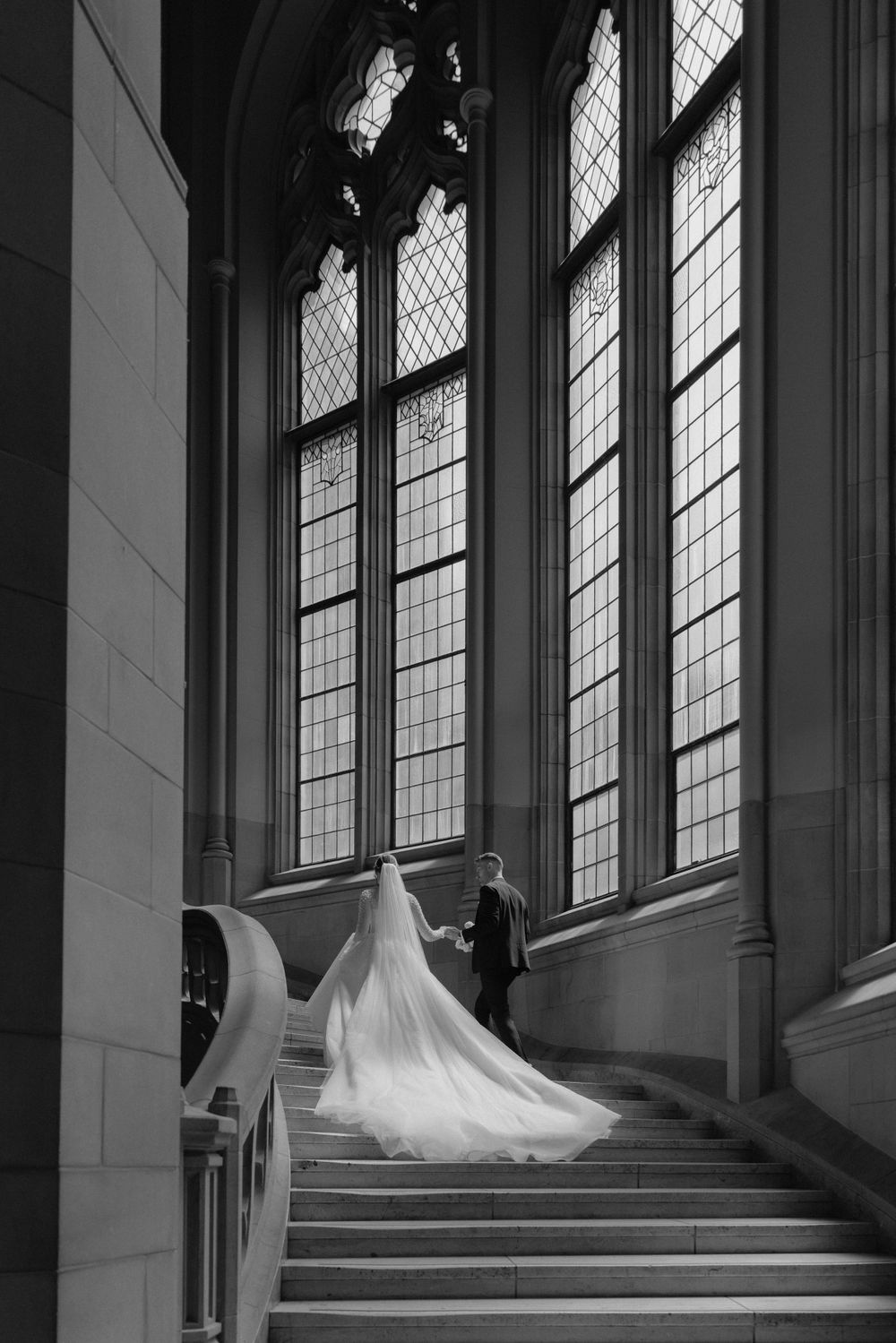 A dramatic black and white wedding photo showing a flowing white dress and veil against gothic church windows.
