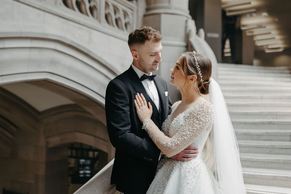Elegant wedding couple embracing by stone archway and classical architecture.