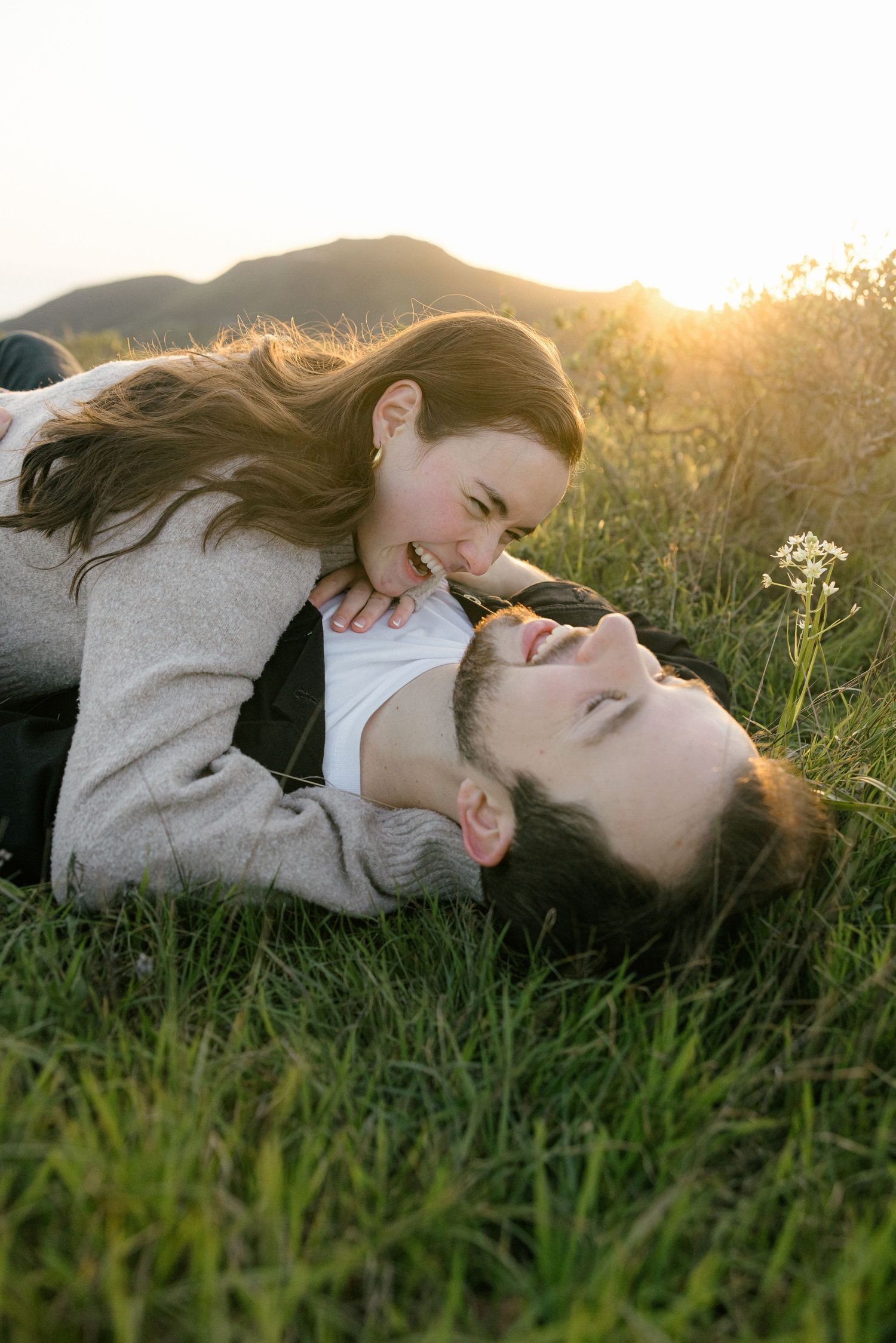 Couple lying in grass field during golden hour sunset.