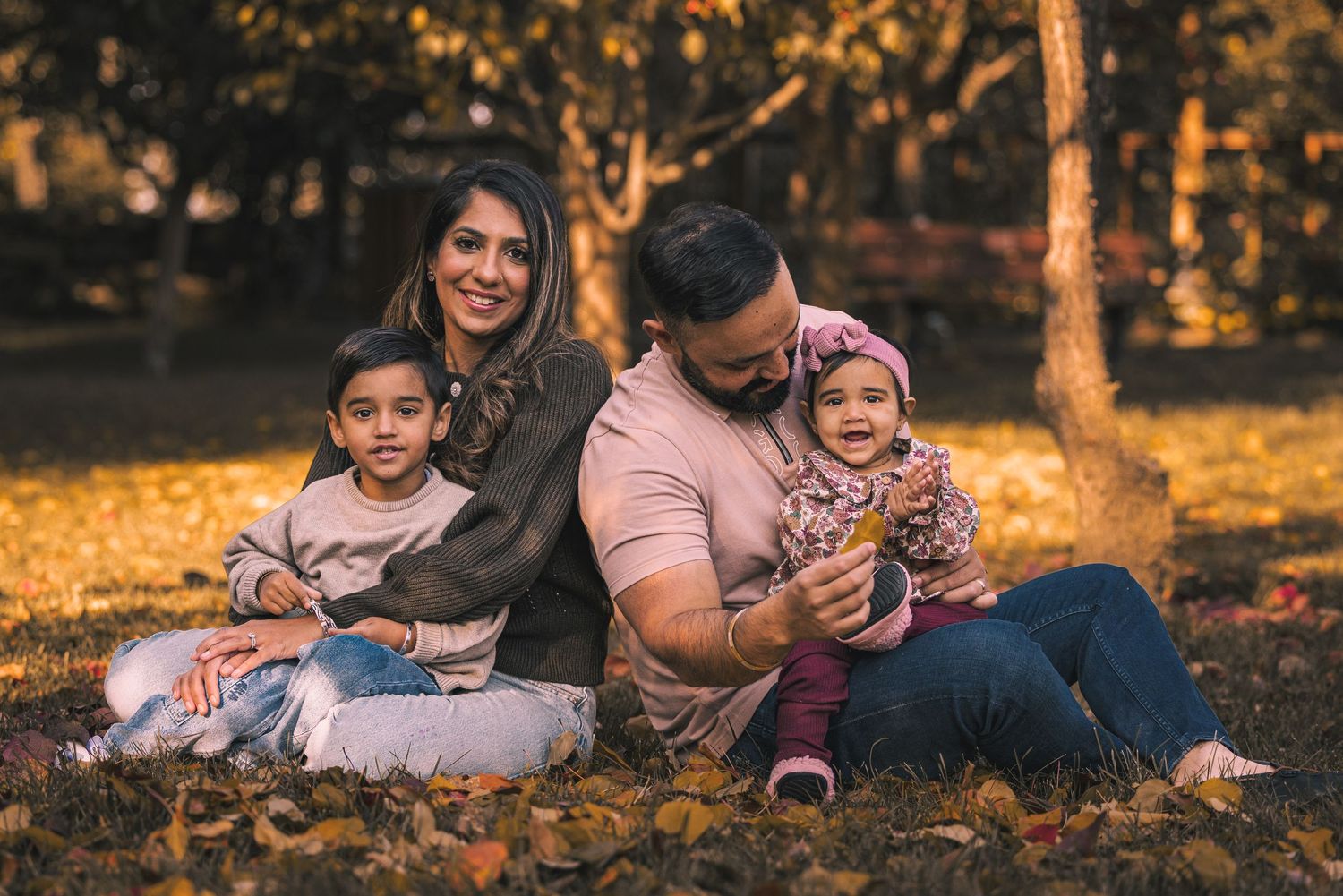 Family relaxing together on fallen leaves during autumn sunset.