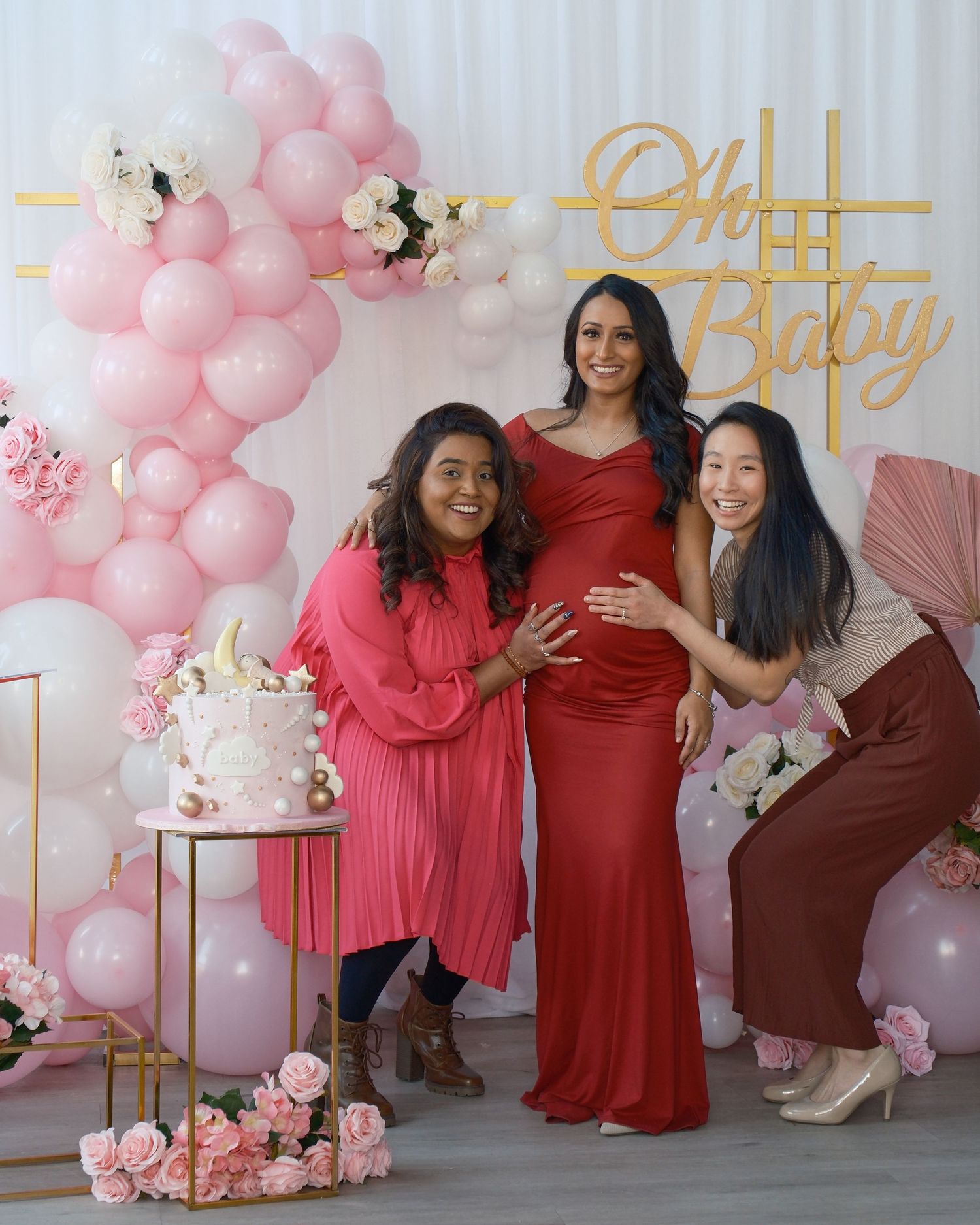 A baby shower scene with pink balloon arch, floral decorations and elegant cake display.
