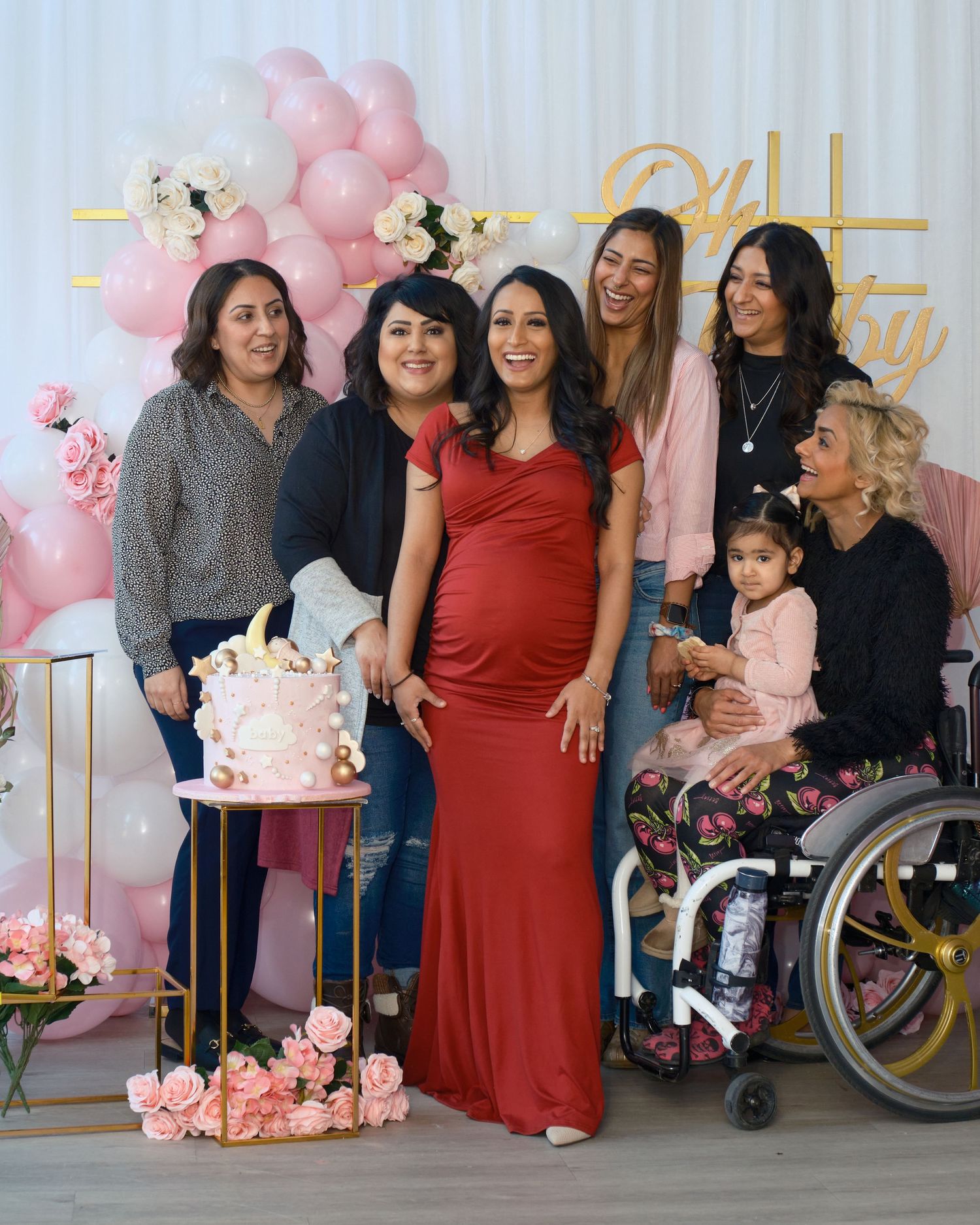 A baby shower celebration with pink balloons, flowers and a decorated cake on display.