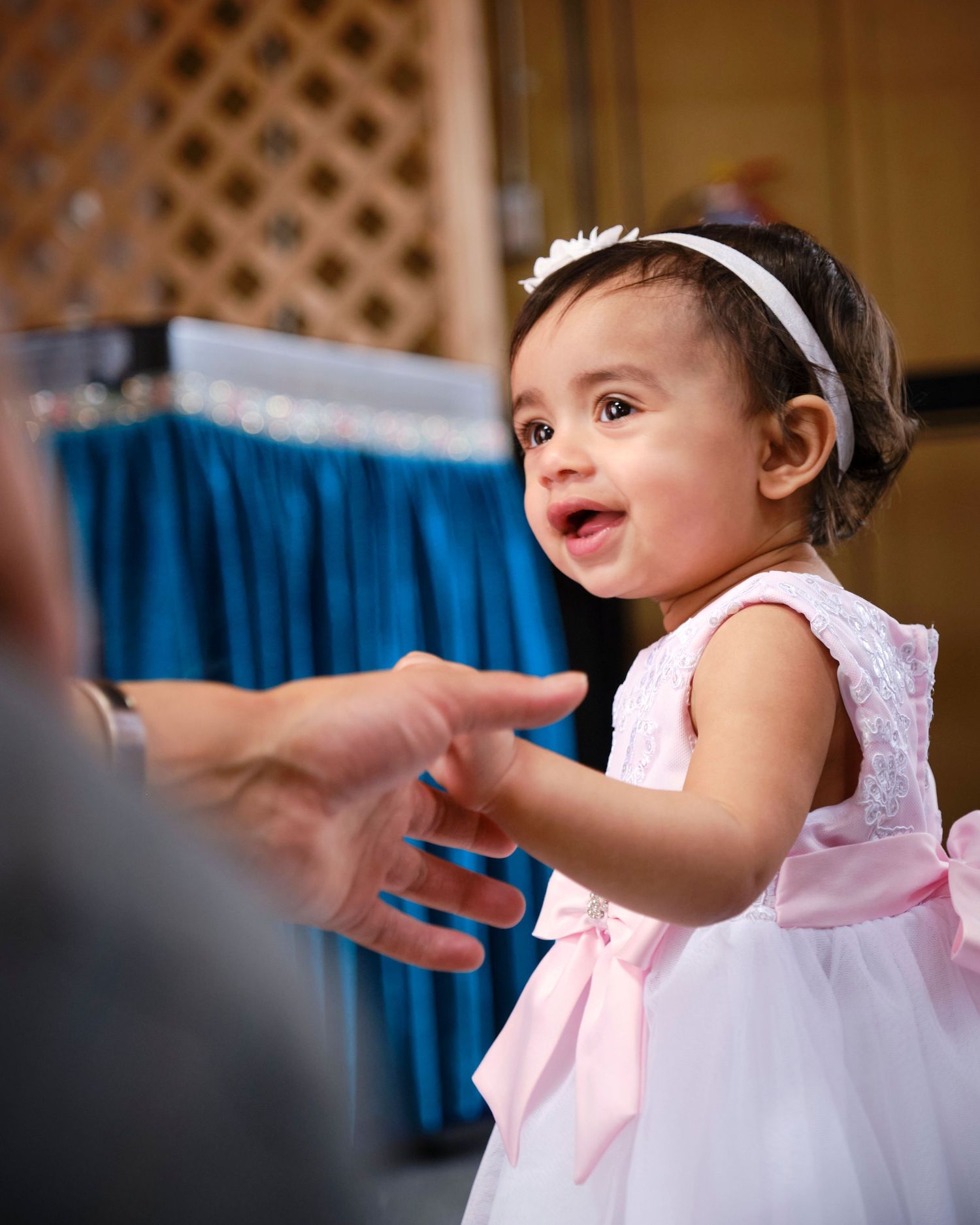 Small child in white dress and headband reaching out with excitement.