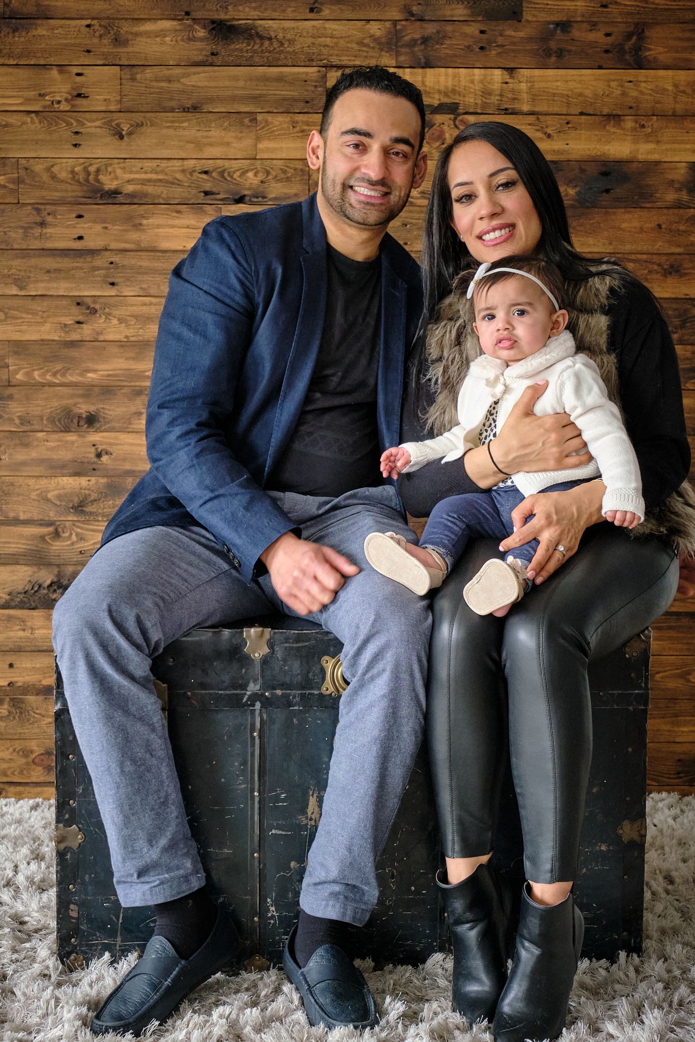 Family portrait against rustic wooden wall background with vintage trunk.