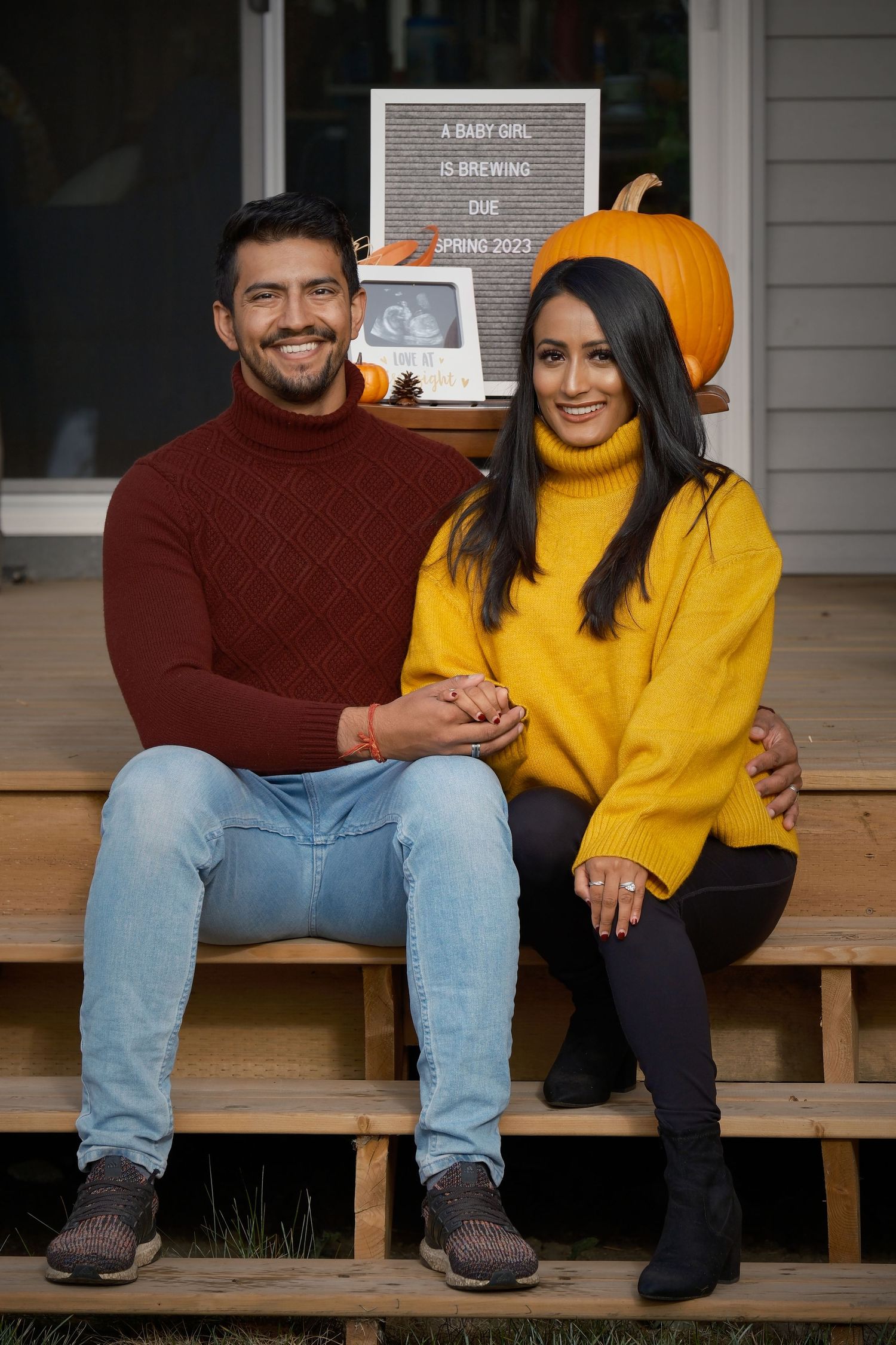 Couple sitting on porch steps with autumn pumpkin decor in background.