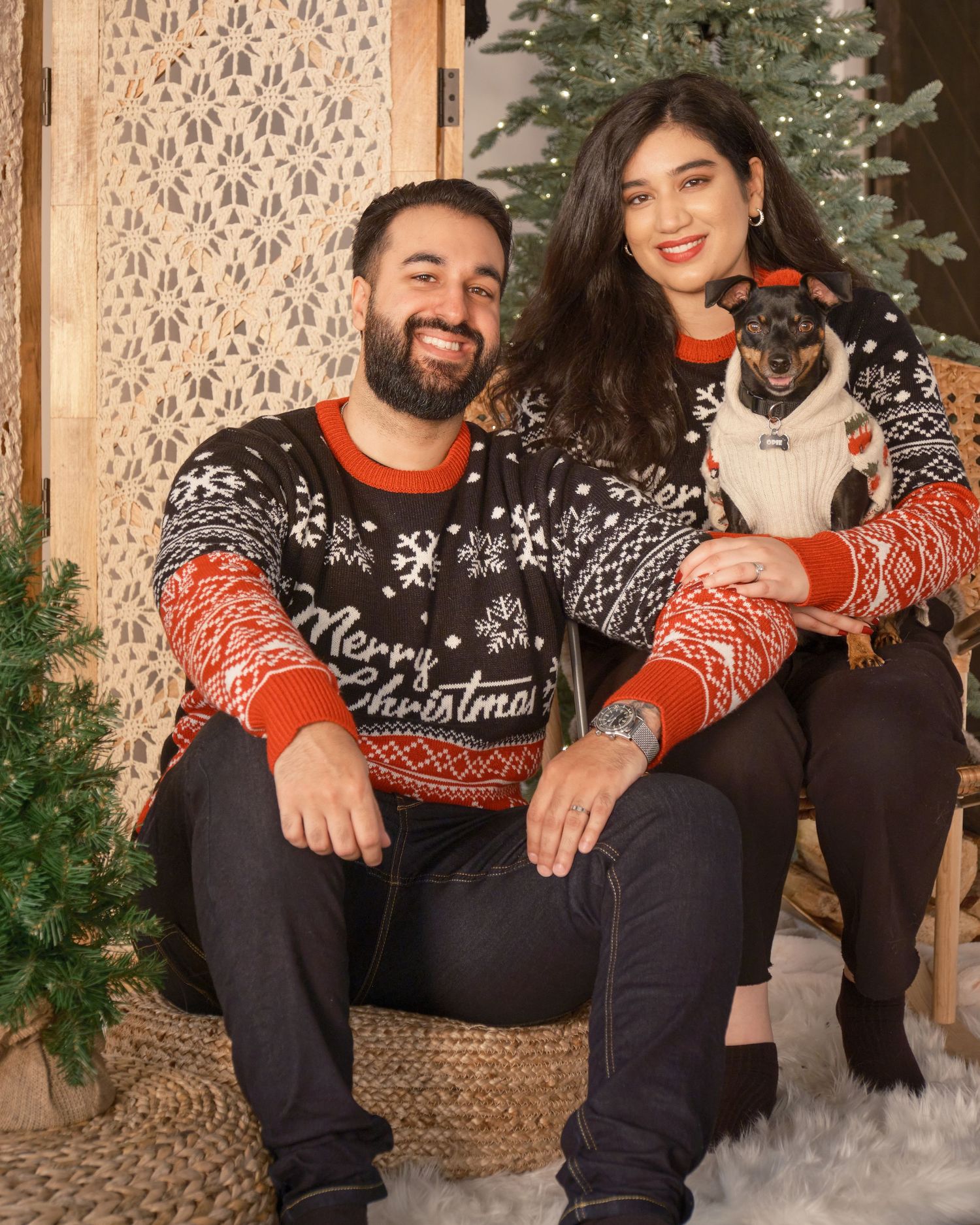 Holiday portrait with Christmas sweaters and small dog next to decorated tree.