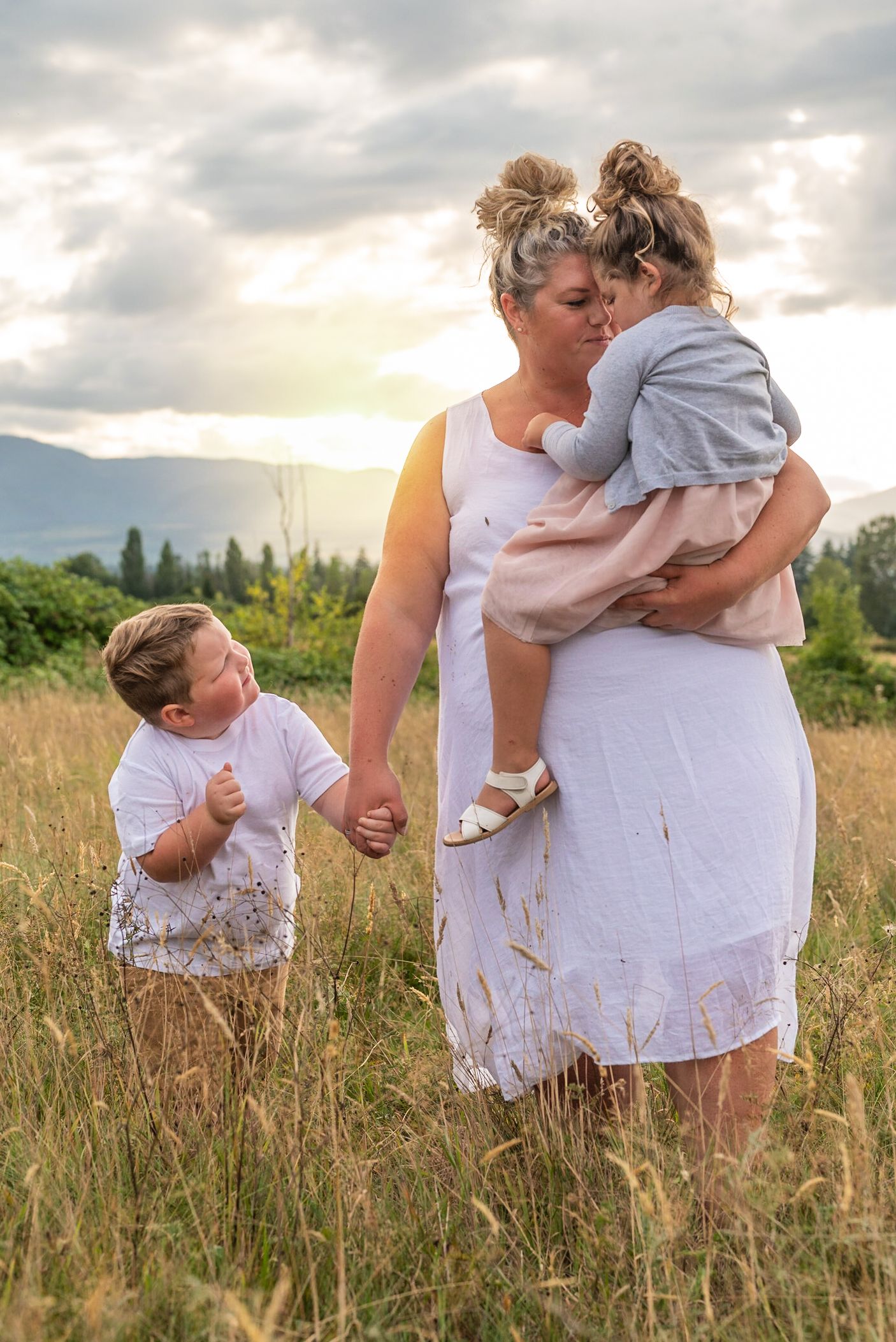 Meadow photoshoot of mom and daughter sharing a snuggle while little brother looks on.