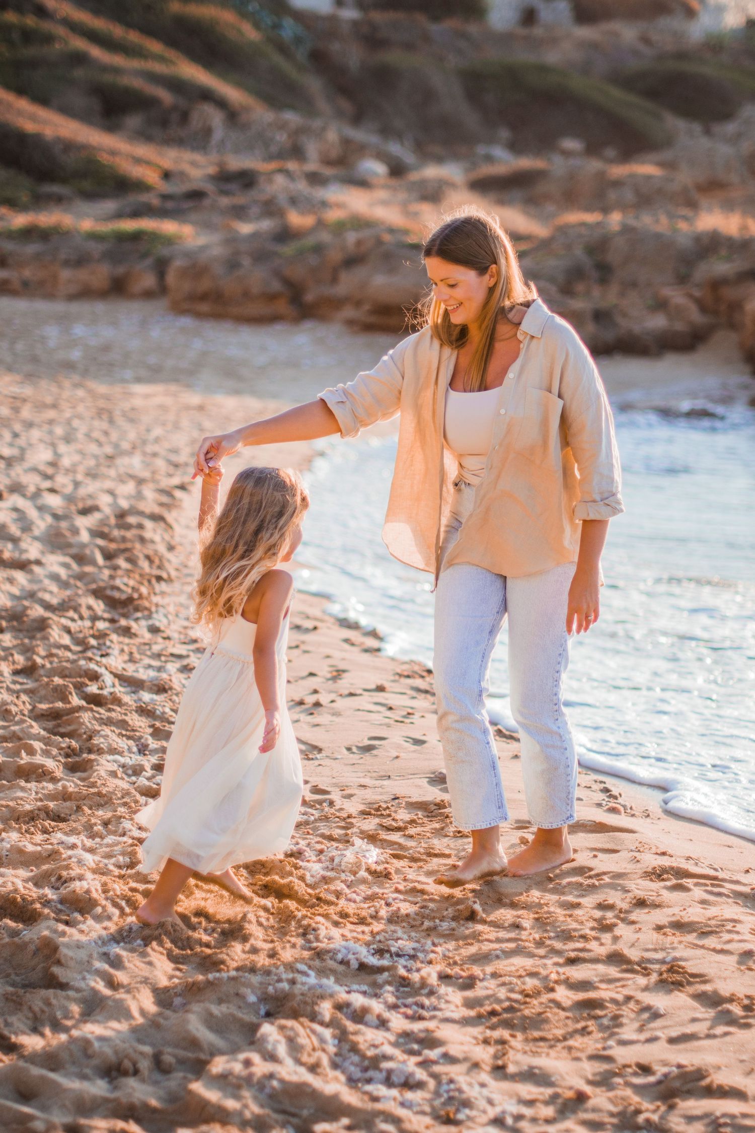 A tender beach moment at sunset with light flowing outfits on sandy shore.