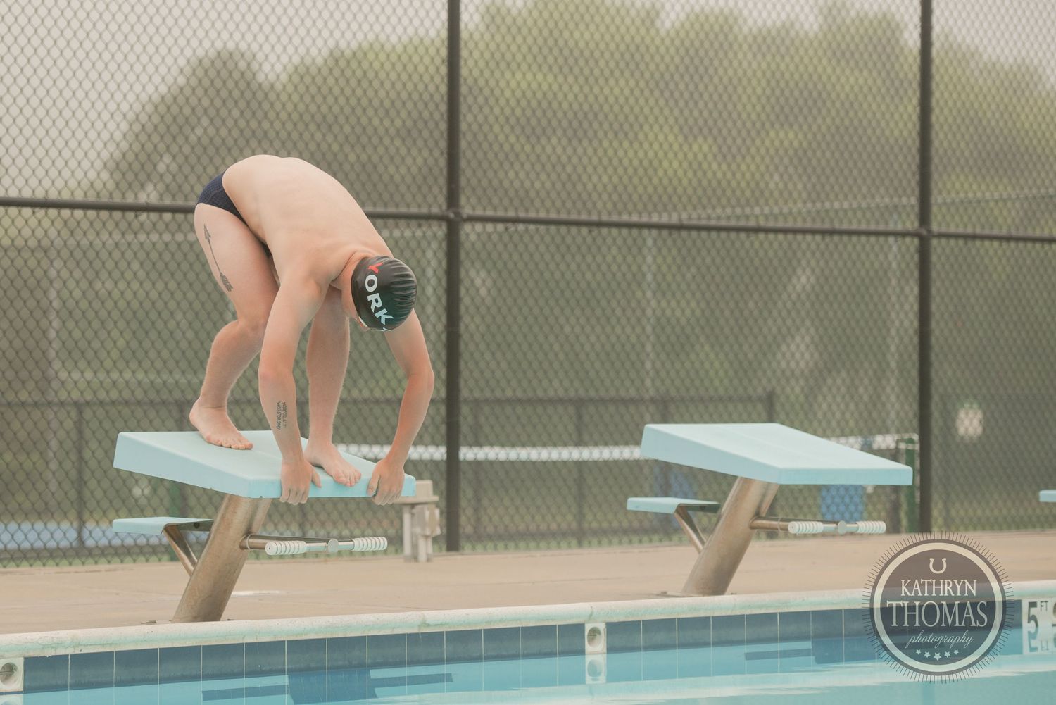 A swimmer prepares to dive from a starting block at an outdoor pool.