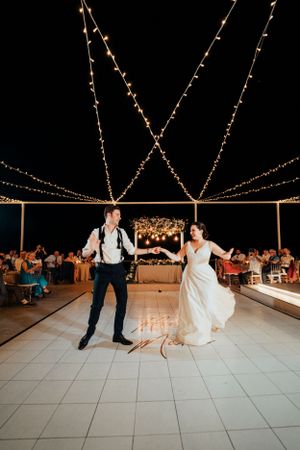 Couple dancing on a tiled floor under string lights at an outdoor wedding reception.