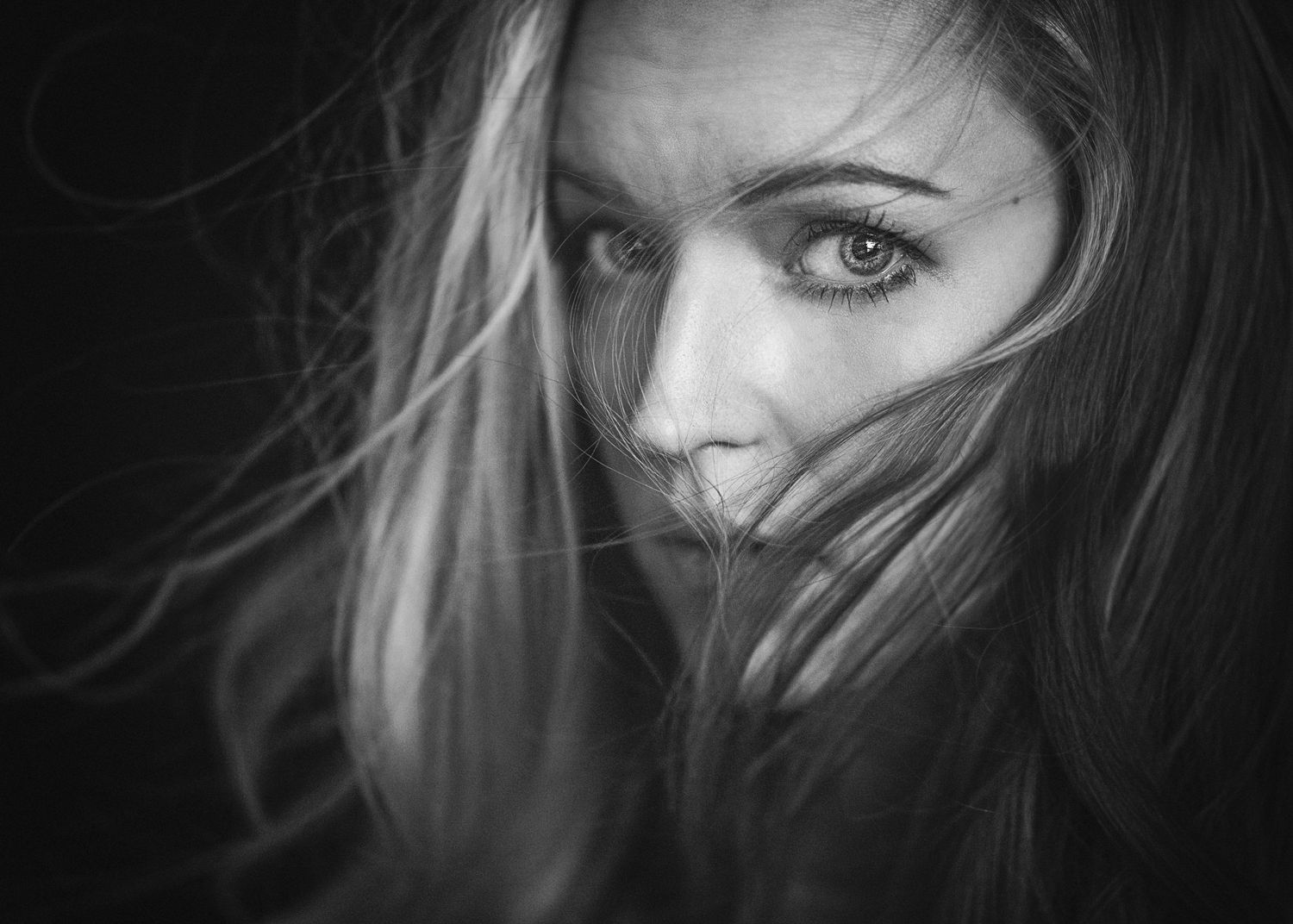 Black and white image of woman with hair blowing across her face as she looks at camera