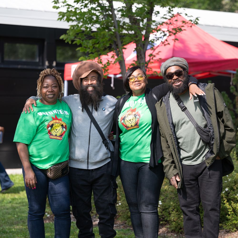 A group of four friends wearing green t-shirts and casual attire pose together outdoors at a community event.