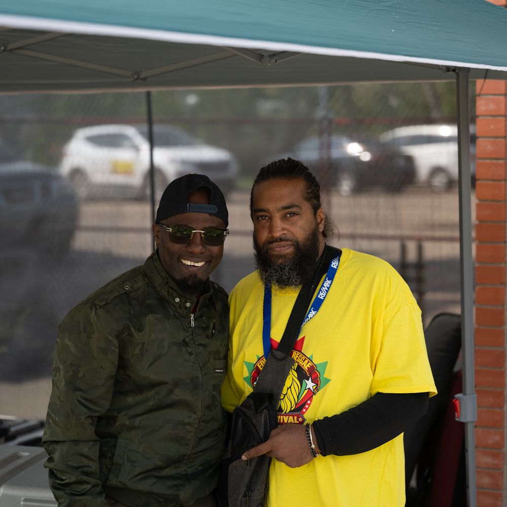 Two people standing together outside a building wearing yellow and dark colored clothing.