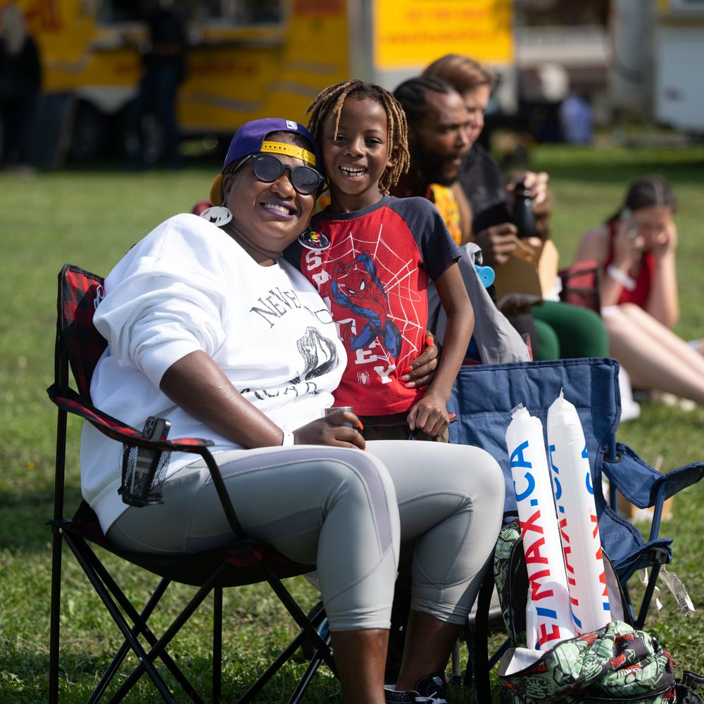 Baseball players relax in folding chairs on the sidelines during a sunny outdoor game.