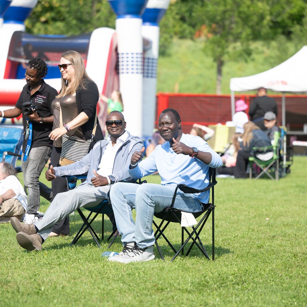 People relaxing in camping chairs on a sunny grassy field during an outdoor event.