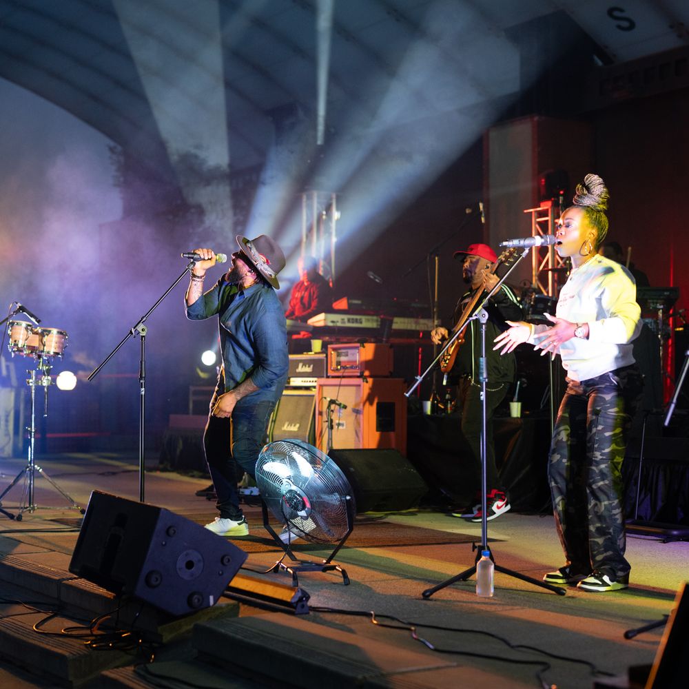 Musicians perform on a dark stage with dramatic lighting and smoke effects during a live concert performance.