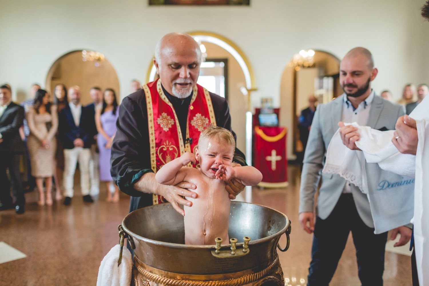 A traditional baptism ceremony taking place at a church with a baptismal font.