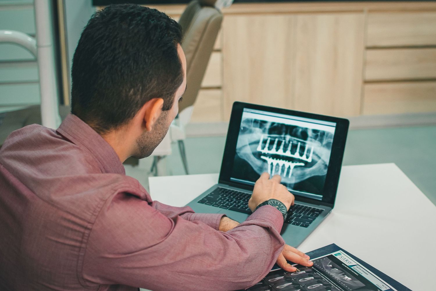 Healthcare provider reviewing dental x-rays on laptop in medical office.
