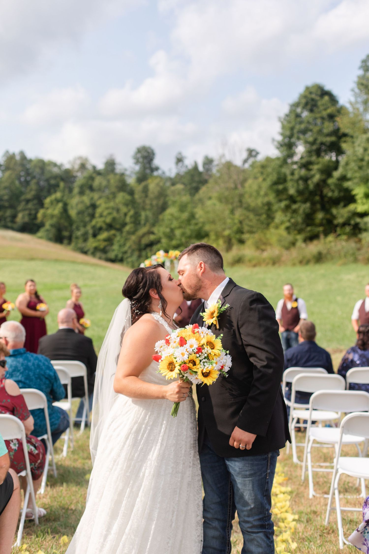 Outdoor wedding ceremony with white chairs and sunflower arch decorations on hillside.