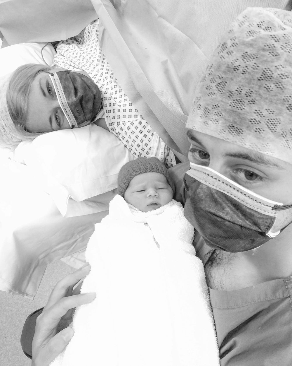 Medical staff in protective gear caring for newborn in hospital setting.