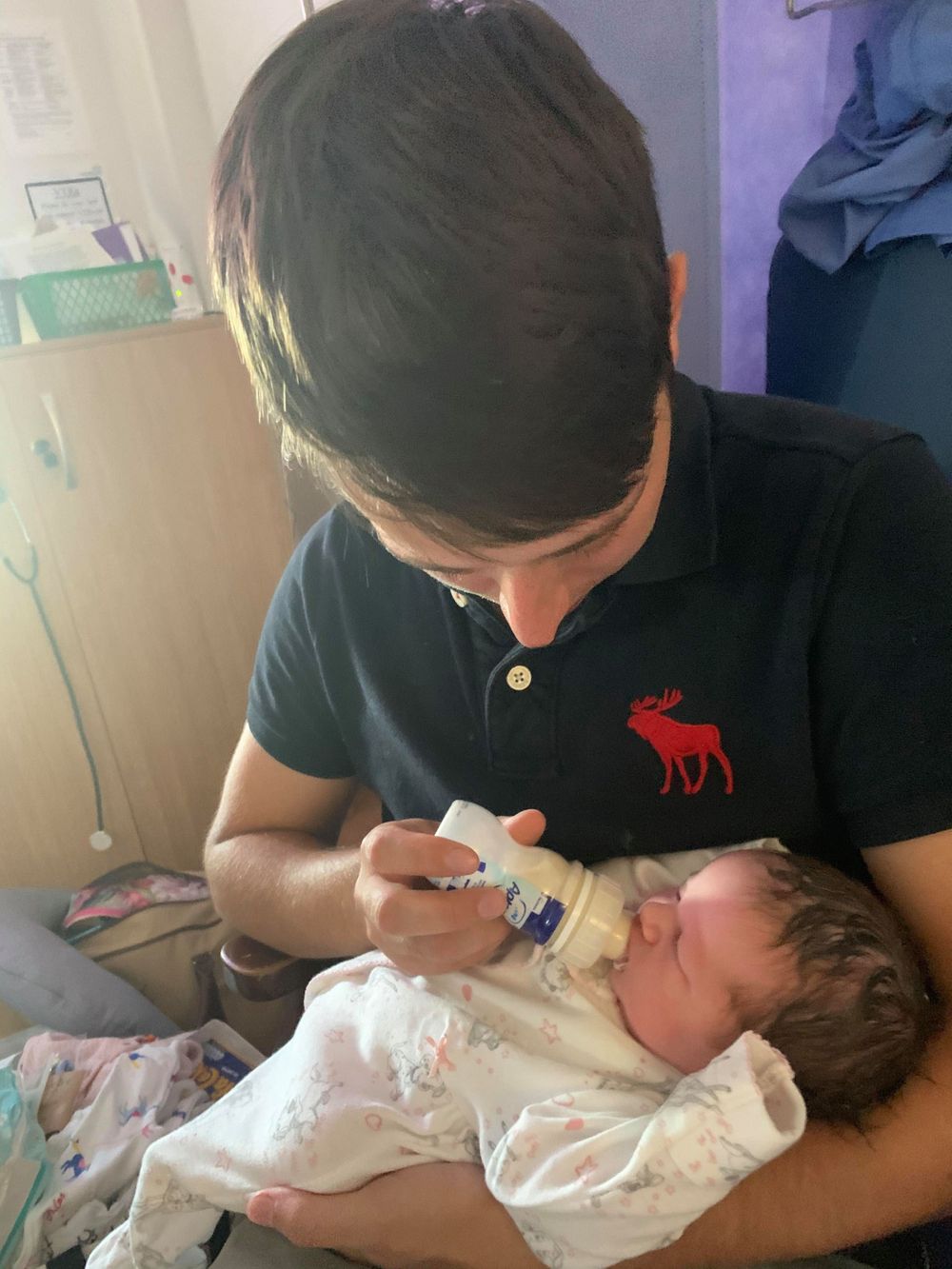 Adult feeding newborn baby with bottle in indoor setting.