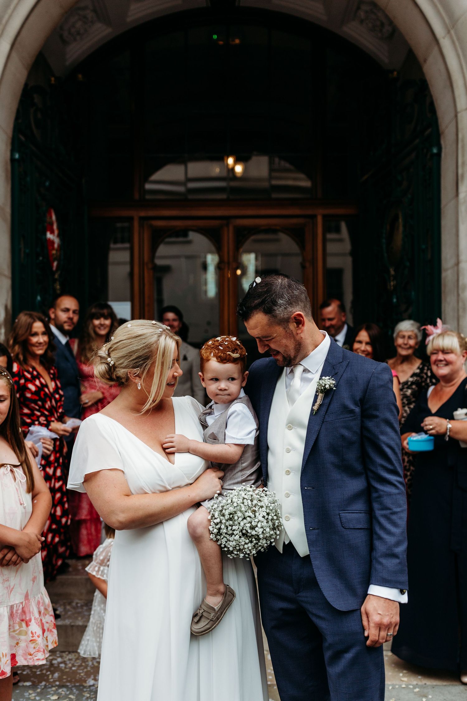 Intimate wedding ceremony moment under stone archway with gathered guests.