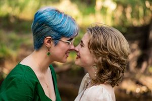Smiling sisters share an intimate moment outdoors with one wearing green and the other in white.