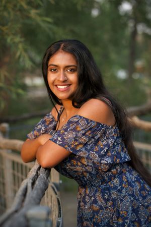 Natural outdoor high school senior portrait of a girl in blue floral off-shoulder dress leaning on railing.