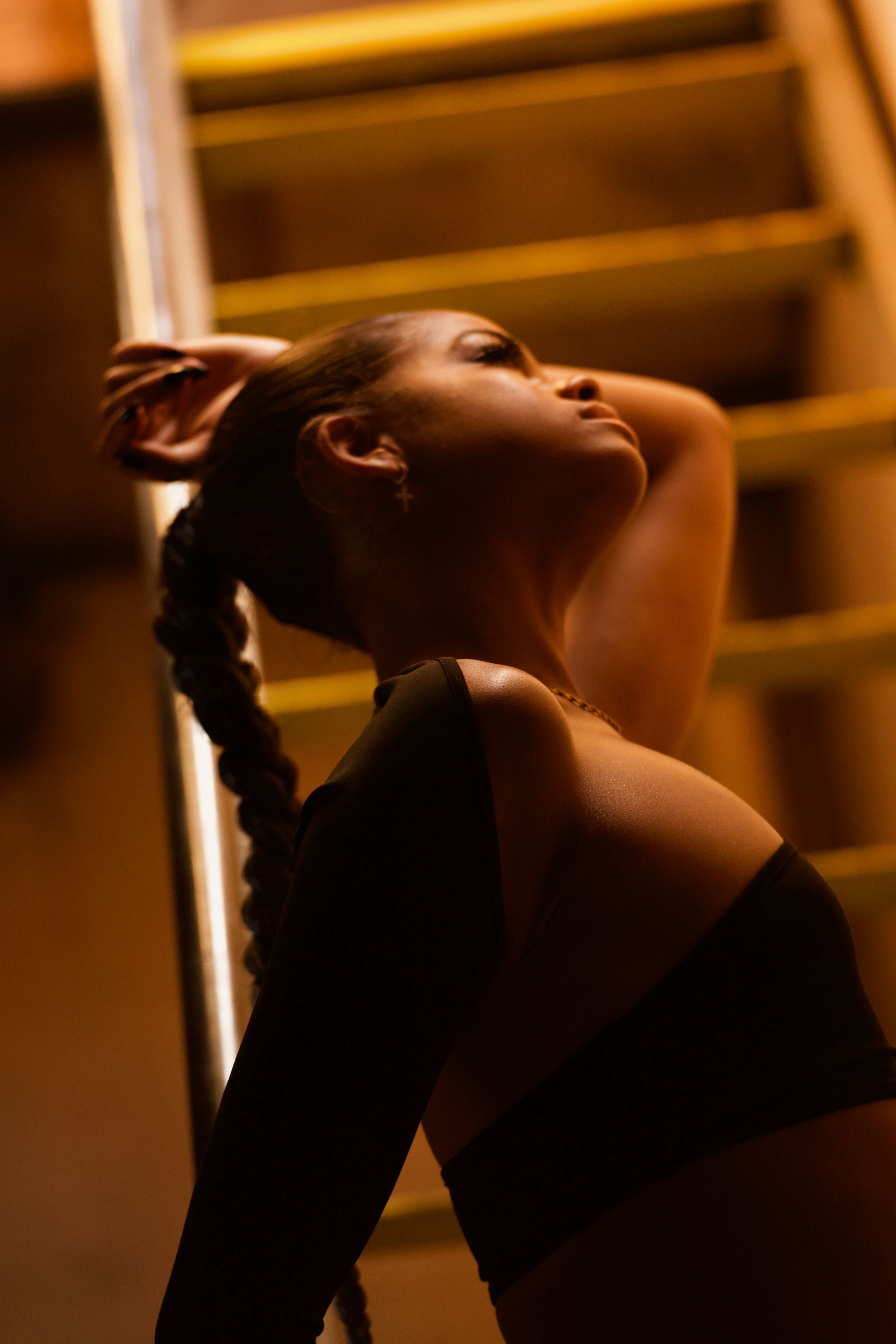 Moody portrait in warm lighting showing silhouette of a woman against wooden stairs.