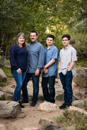 A family of four poses together outdoors on rocky terrain surrounded by trees.