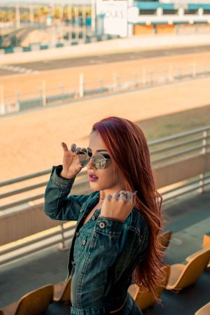Fashion portrait at stadium with sunglasses and denim jacket in warm sunset lighting.