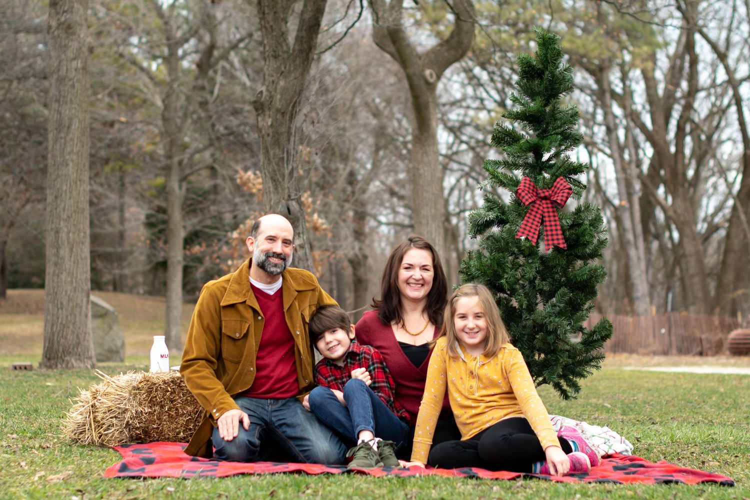 Festive holiday portrait session with family on red blanket near decorated Christmas tree.