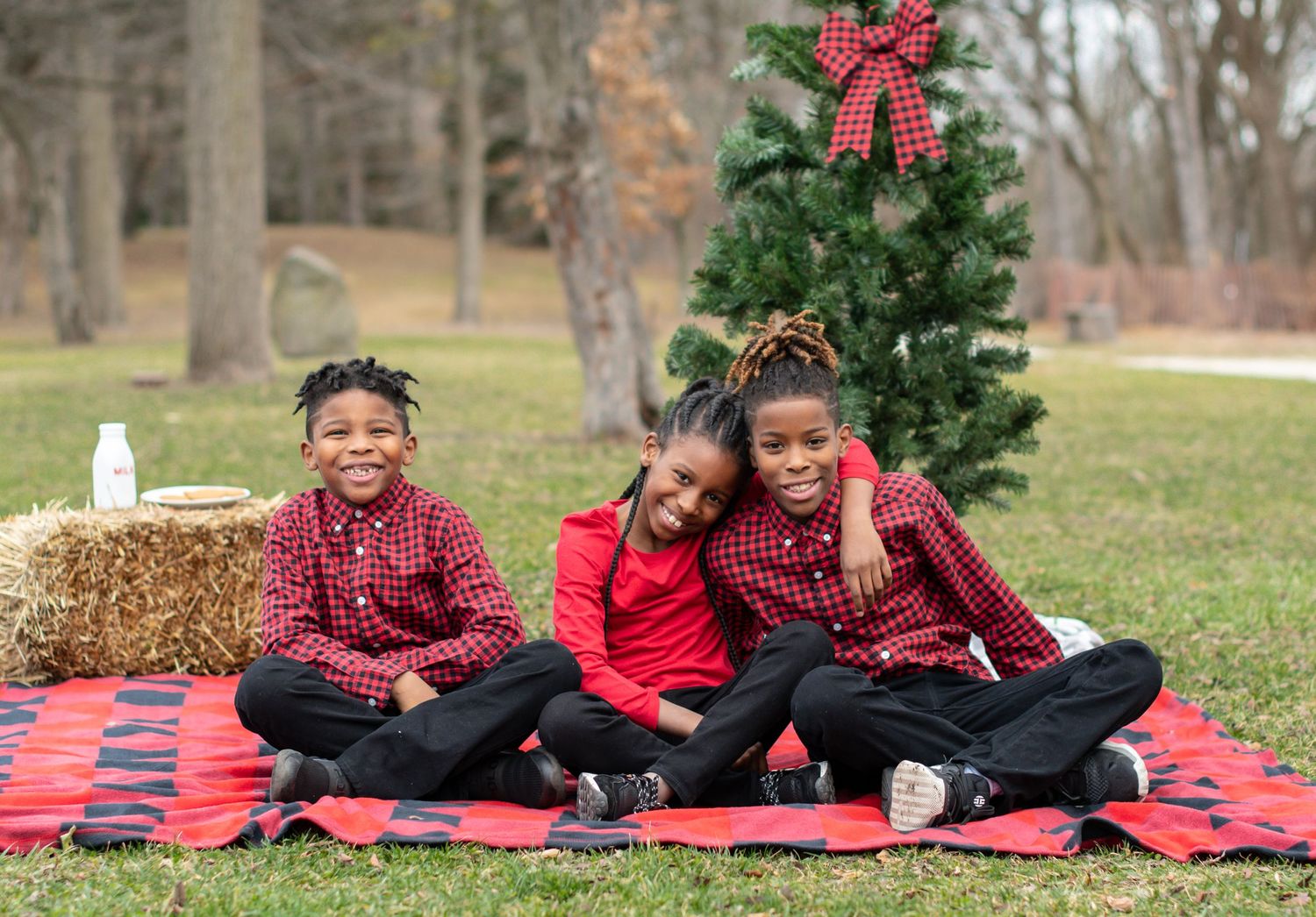 Family Christmas photo with matching red and burgundy outfits on picnic blanket outdoors.