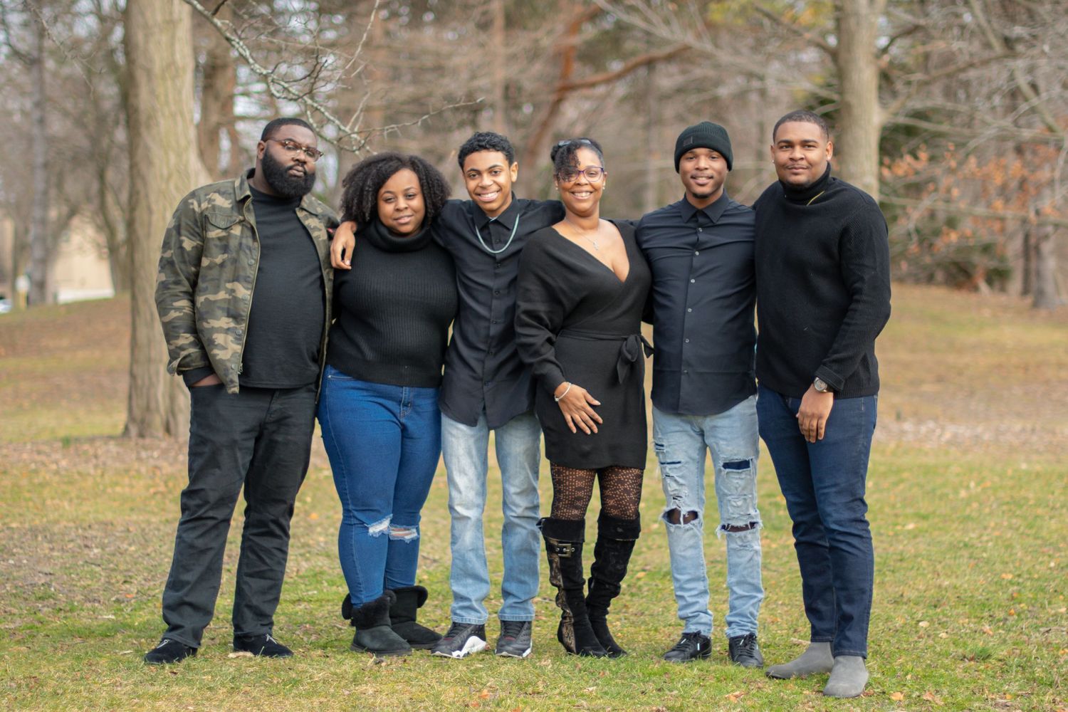 Family members pose together on grass in casual winter clothing.