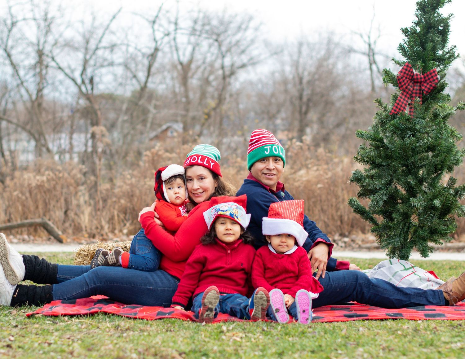 Family group relaxes together on a red blanket for holiday photos outdoors.