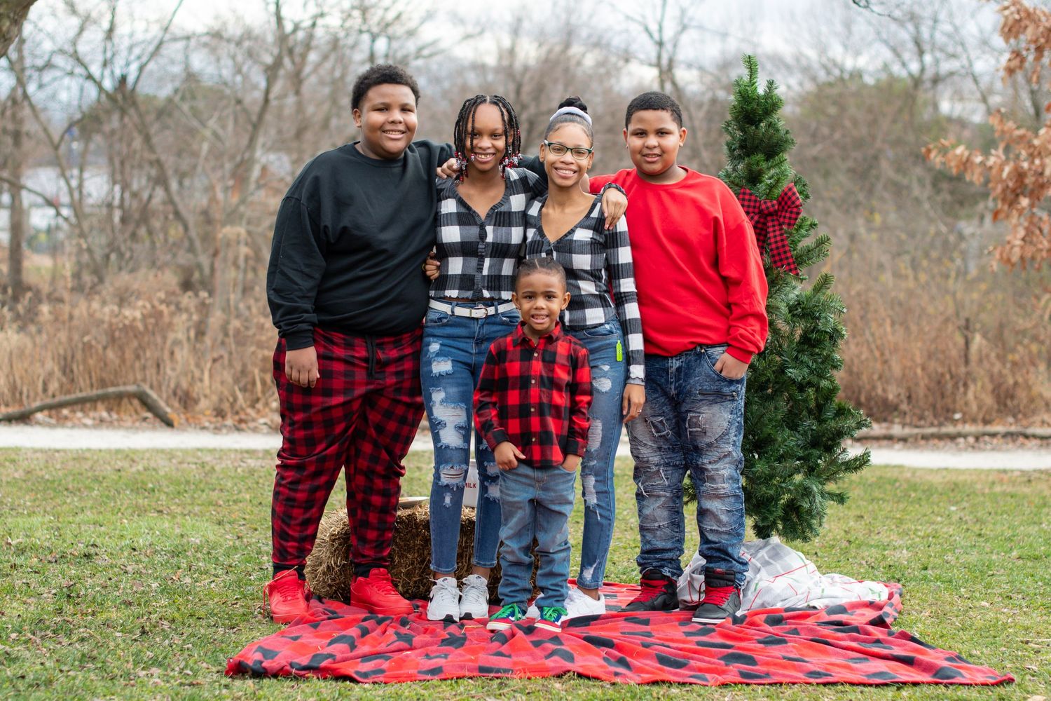 Family group stands together outdoors near an evergreen tree for holiday photos.