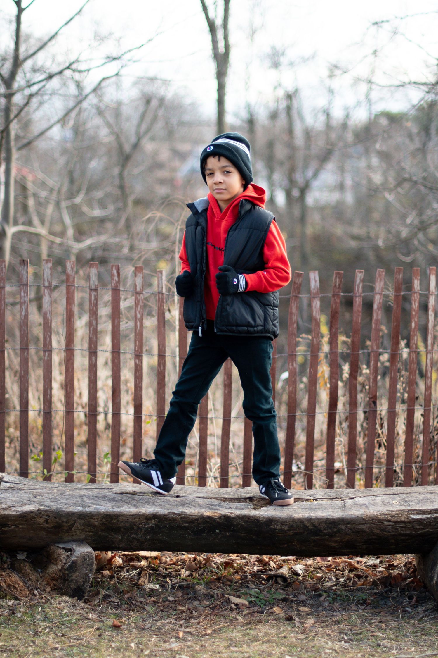 Child in winter clothing balancing and walking on a wooden log in a park.