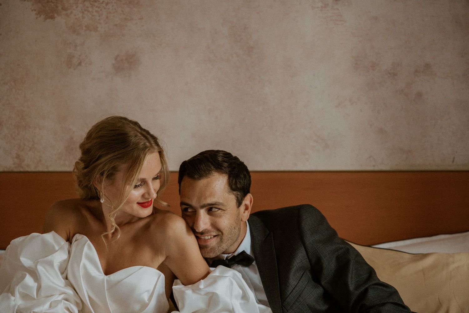 A romantic wedding photo of newlyweds sharing an intimate moment on a bed.