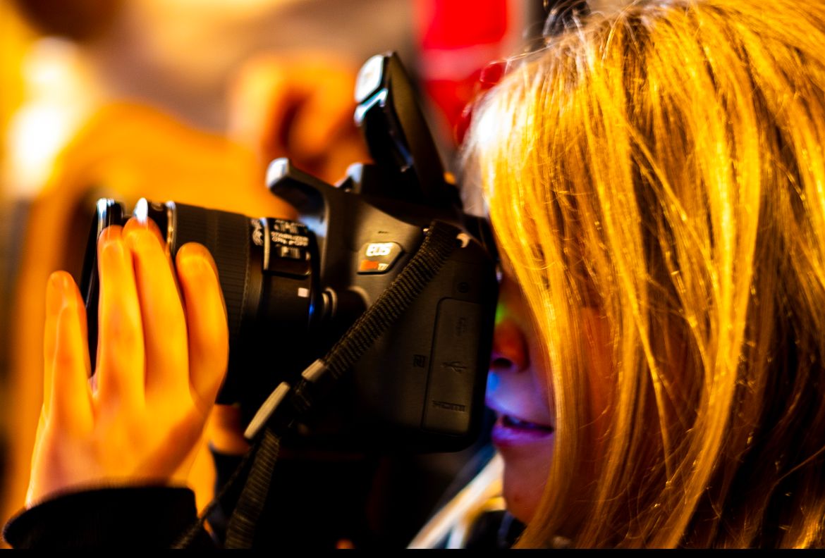 Close-up view of someone using a professional DSLR camera with bokeh background effects.
