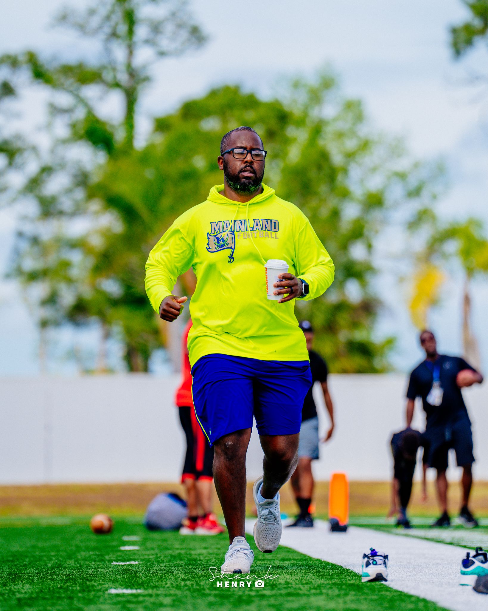 Athlete in neon yellow sweatshirt running drills on sports field.