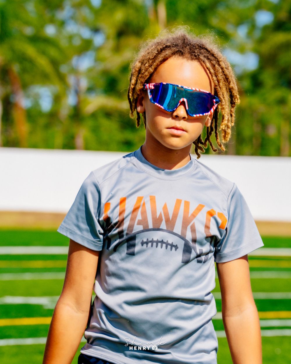 Young athlete in grey Hawks football shirt and sporty sunglasses on football field.