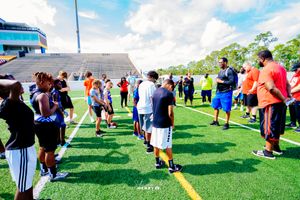 Athletes jump to catch football on sports field under blue sky.